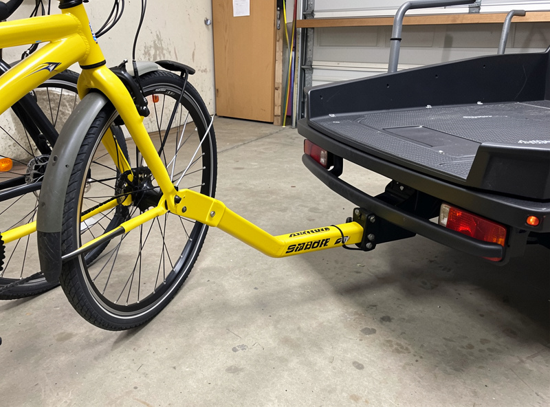 A child trailer hitched behind a commuter e-bike beside a longtail cargo e-bike for comparison