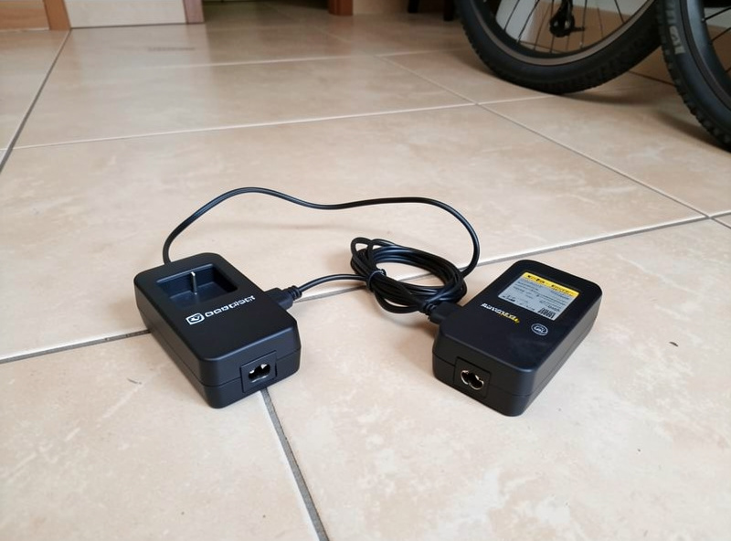 E-bike battery charging on a tiled floor indoors next to the original charger