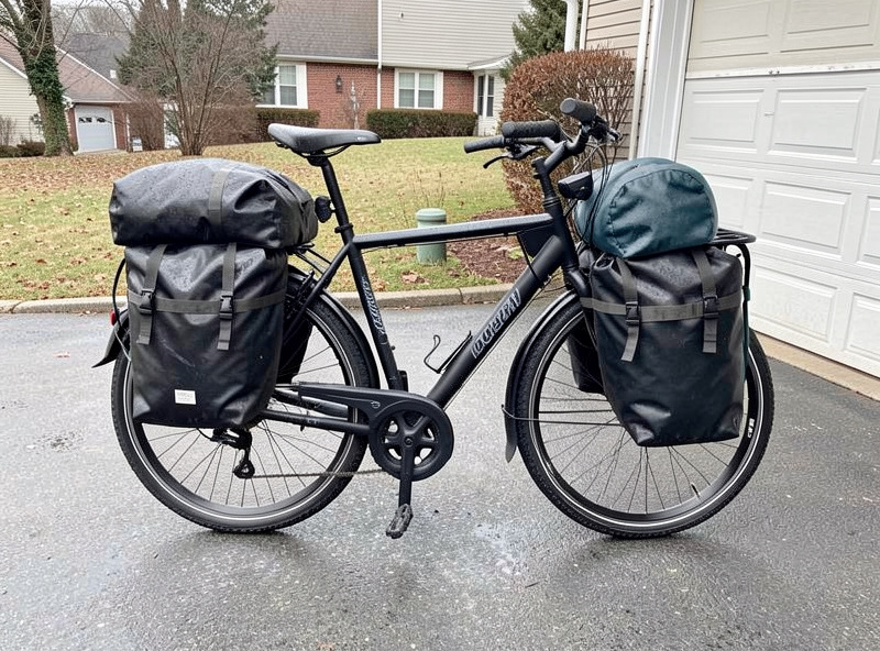 A commuter e-bike loaded with full fenders, a rated rear rack and two packed waterproof panniers, ready for a wet winter ride