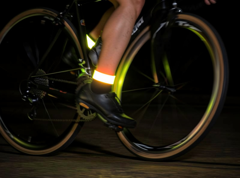 Retroreflective ankle bands on a cyclist mid-pedal stroke catching light in the dark
