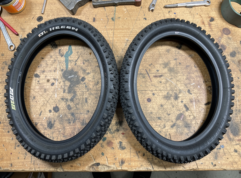 Two studded e-bike tires of different widths laid side by side for comparison